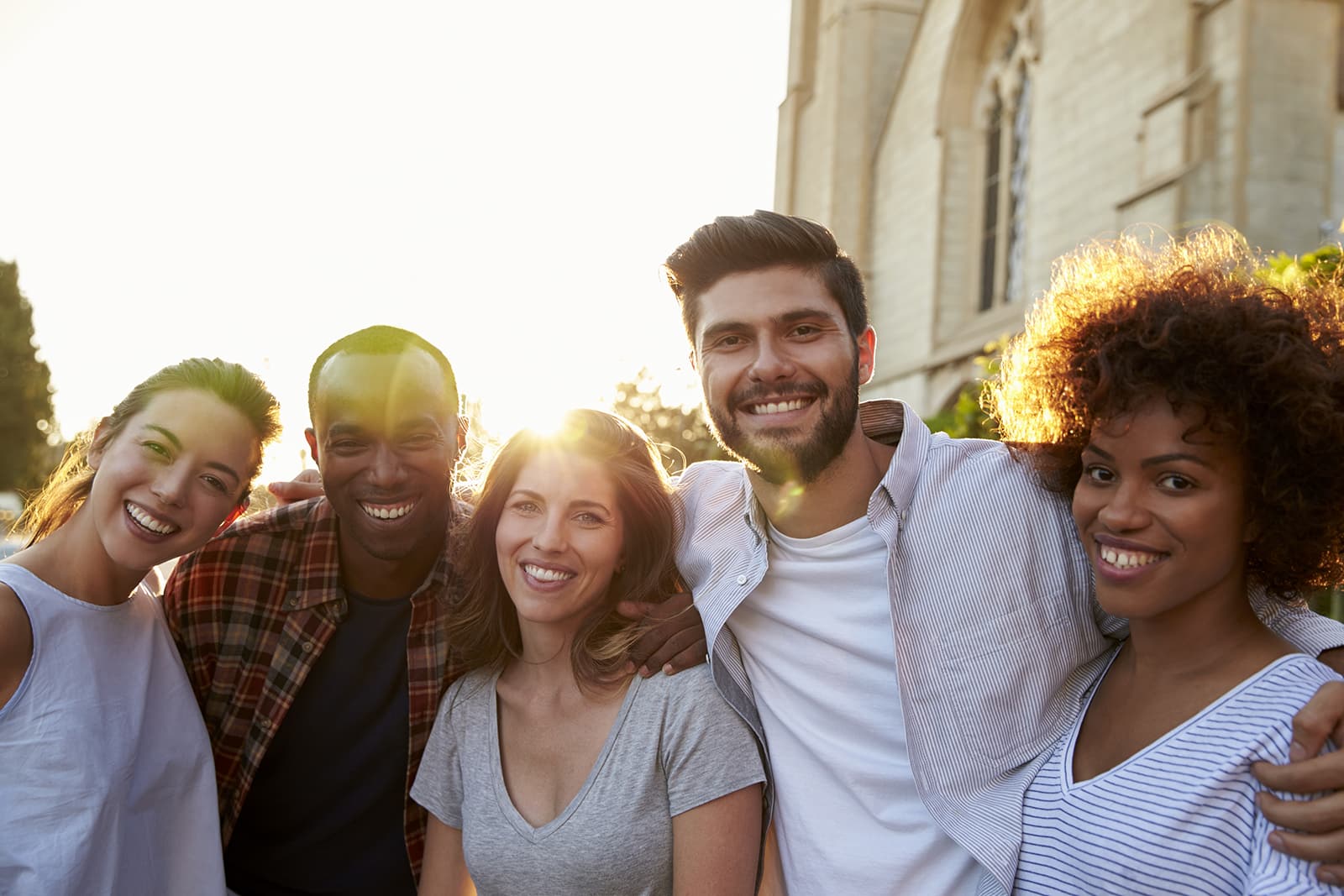 Group of smiling young adult friends embracing in the street